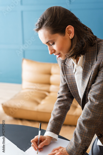 Beautiful brunette woman standing at desk, holding pen and working with documents.