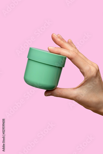 Woman hand showing cream product. Cosmetic product branding mockup. Daily skincare and body care routine. Female hand holding  cosmetic product mockup on a light pink background. Close up.