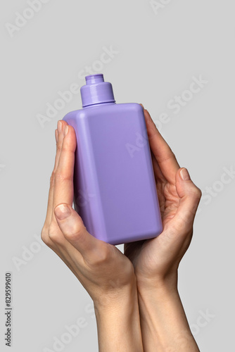 Woman hand showing a package of bath foam or shampoo. Cosmetic product branding mockup. Daily skincare and body care routine. Female hand holding  cosmetic product mockup on a light gray background. 
