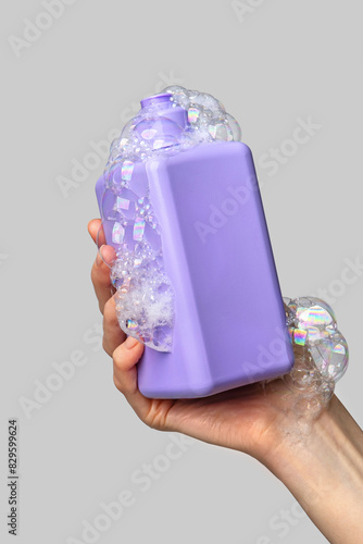 Woman hand showing a package of bath foam or shampoo. Cosmetic product branding mockup. Daily skincare and body care routine. Female hand holding  cosmetic product mockup on a light gray background. 