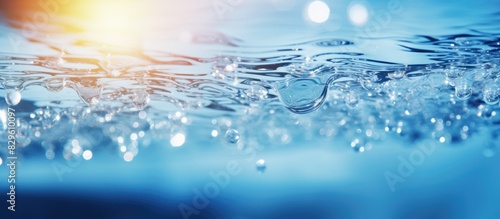 A trendy abstract nature background featuring de focused blurred transparent blue water surface with splashes bubbles and water waves sparkling in sunlight next to copy space image