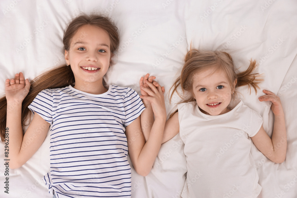 Cute little sisters on bed, top view Cute little sisters on bed, top view