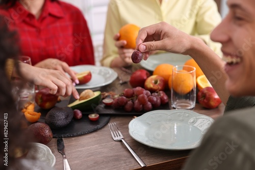 Vegetarian food. Friends eating fresh fruits at wooden table indoors, closeup