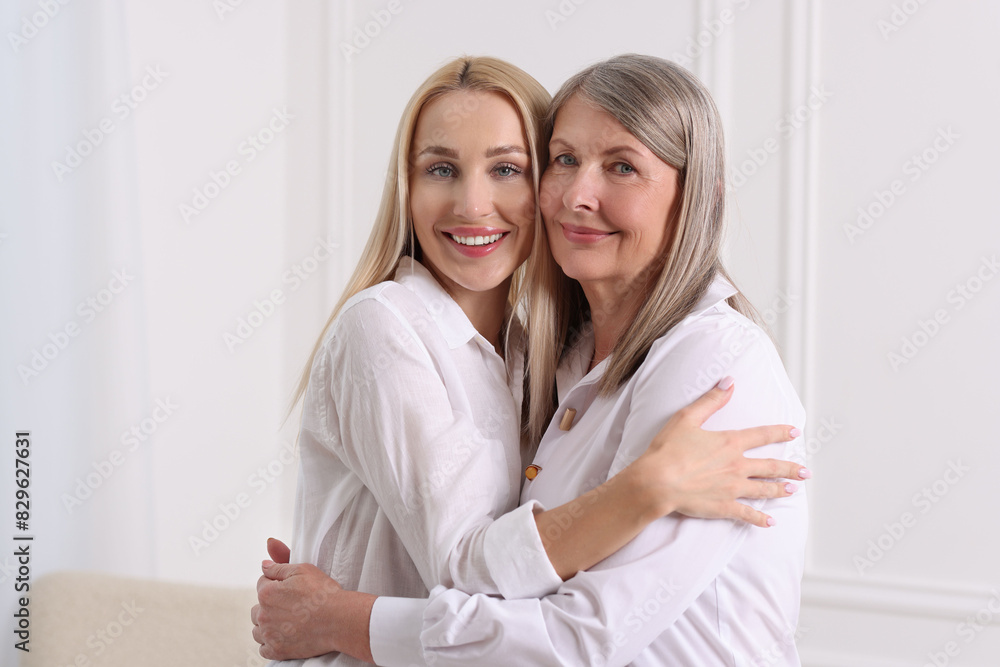 Family portrait of young woman and her mother near white wall Family portrait of young woman and her mother near white wall