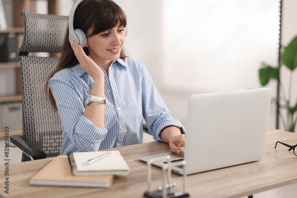 Woman in headphones watching webinar at wooden table in office Woman in headphones watching webinar at wooden table in office