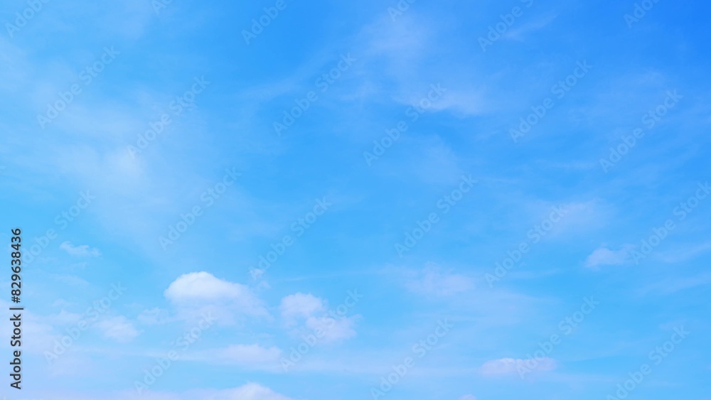 Naklejka premium A bright blue sky with a few scattered, fluffy white clouds. The sky appears clear and vast, suggesting a beautiful and serene day. The soft, light clouds add a gentle texture to the expanse of blue. 