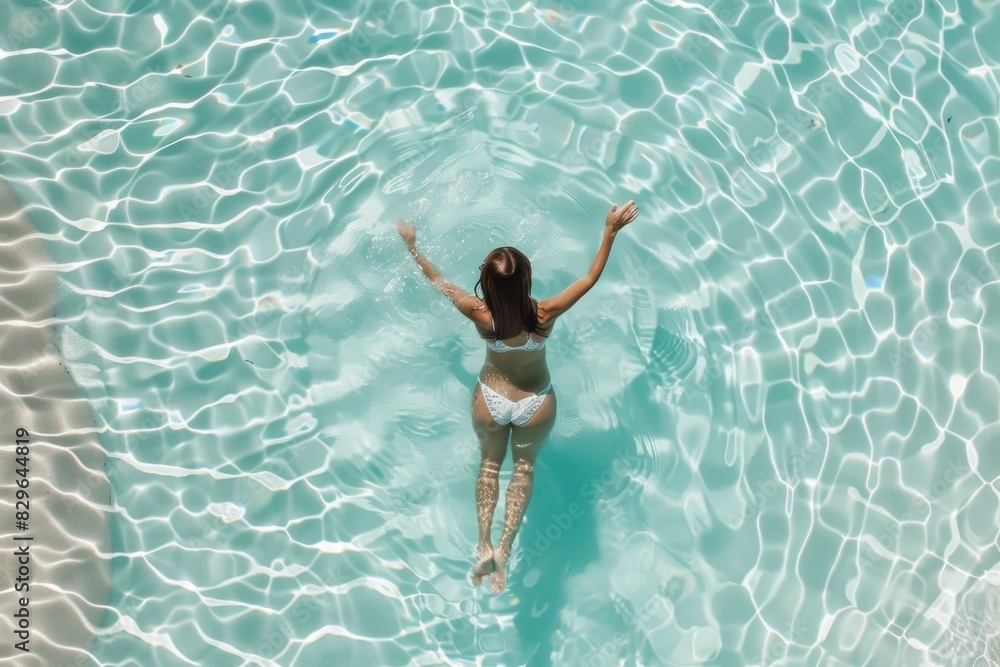 A black woman in an elegant swimsuit swims in a crystal-clear pool from an overhead perspective