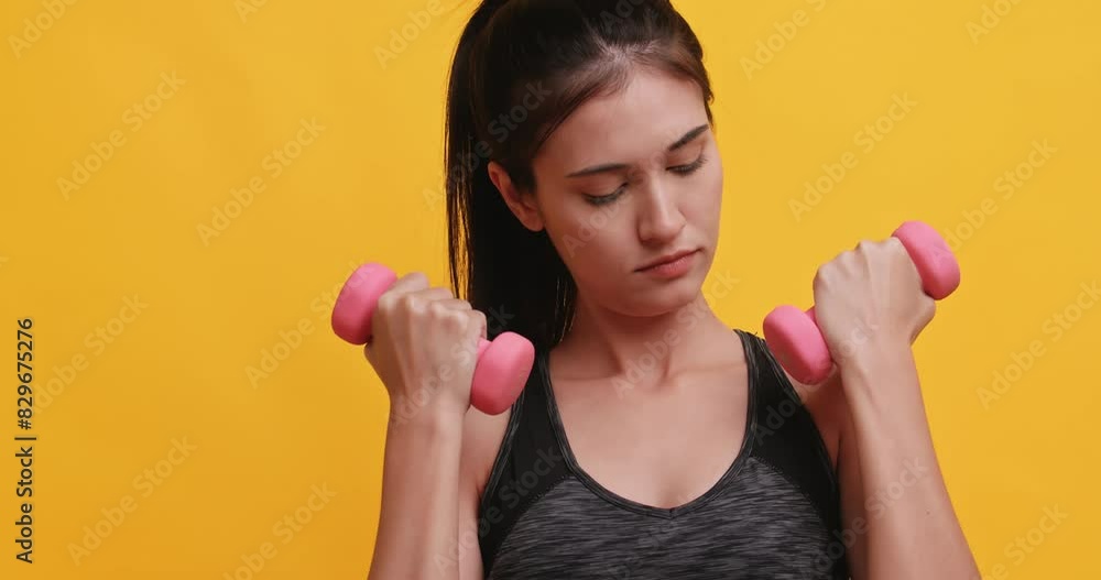 Young sportswoman shows off her physical strength by lifting dumbbell. Isolated on yellow background in studio. Young sportswoman shows off her physical strength by lifting dumbbell. Isolated on yellow background in studio.