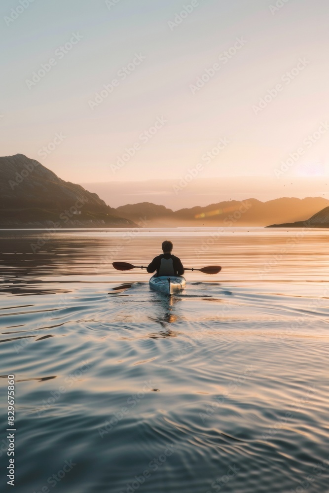 Fototapeta premium Serene Kayaker Enjoys Golden Sunset on Tranquil Mountain Lake