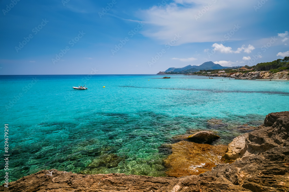 Fototapeta premium A beautiful clear turquoise Mediterranean sea with a lonely boat and rocks near the coast - a serene coastal scene from Mallorca