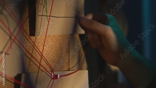 Close-up of board with notes and threads. Stock footage. Man is investigating and fixing evidence on board. Man checks photos and notes on research board