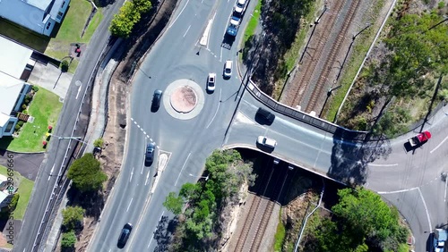Pan over landscape cars driving around roundabout main road street with train line bridge infrastructure transportation Ourimbah Australia drone aerial photo