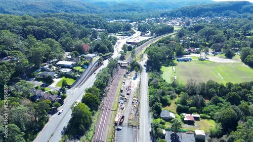 Landscape view of railway tracks train line and cars driving on road street in main town bushland suburb neighborhood Ourimbah Australia drone aerial photo