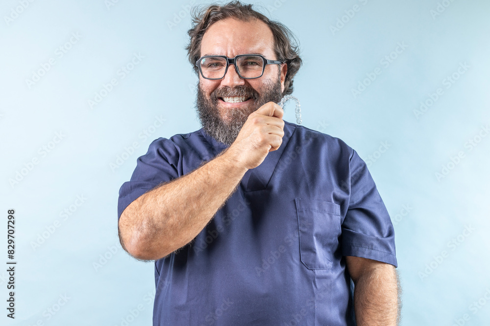 smiling dentist adult man with glasses and beard on blue background looking at camera and showing invisible dental corrector smiling dentist adult man with glasses and beard on blue background looking at camera and showing invisible dental corrector