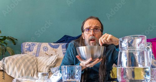 A man is eating from a bowl looking with interest at something in front of him. The man seems totally absorbed in what he is seeing.