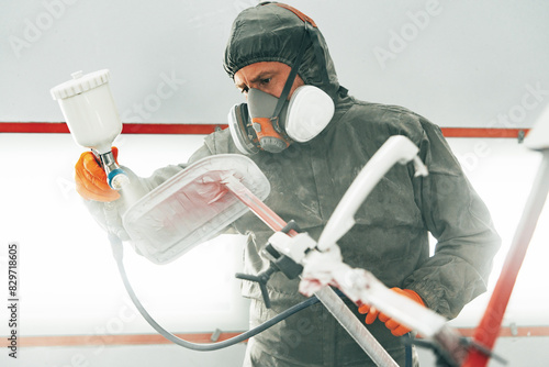 Male painter in respiratory mask and protective suit painting car with spray gun in car service photo