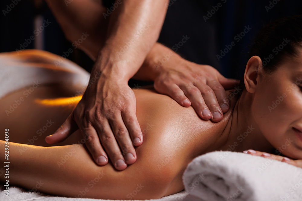 A young brunette woman receives a professional back massage in a spa salon. A beautiful naked lady in a towel with perfect skin gets a relaxing massage. The concept of luxury professional massage. A young brunette woman receives a professional back massage in a spa salon. A beautiful naked lady in a towel with perfect skin gets a relaxing massage. The concept of luxury professional massage.