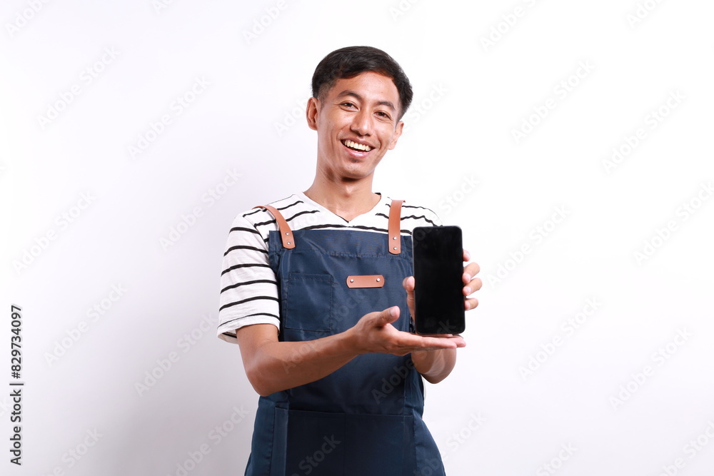 Happy smiling asian barman in blue apron showing blank smartphone screen over white background Happy smiling asian barman in blue apron showing blank smartphone screen over white background