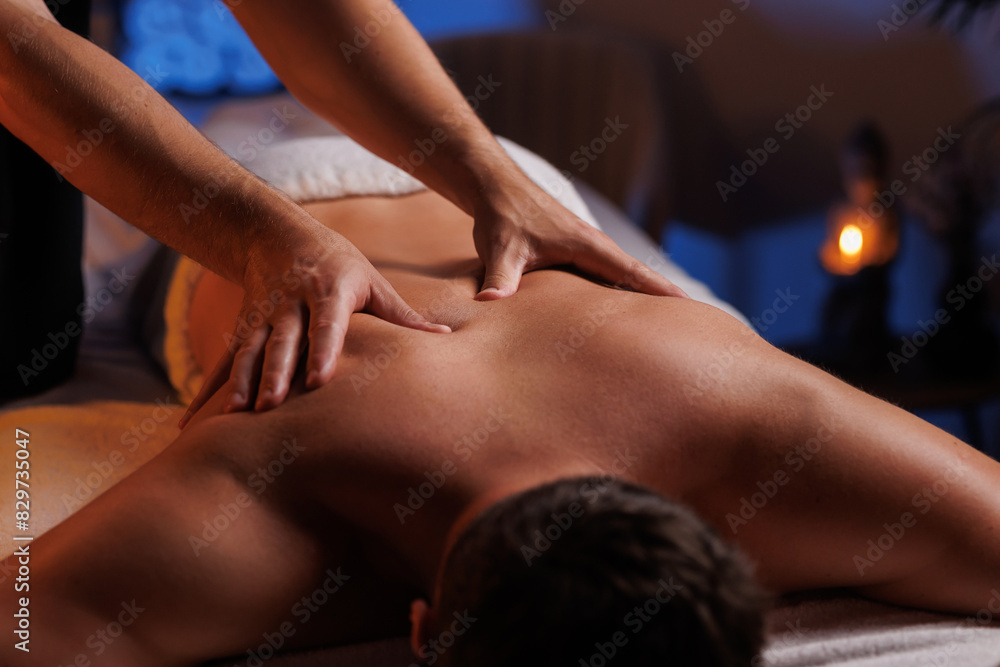 Fototapeta premium Physiotherapist massaging male patient with damaged shoulder muscle, treating sports injuries. Relaxing professional shoulder massage in cozy atmosphere, reboot on the weekend, end of difficult week.