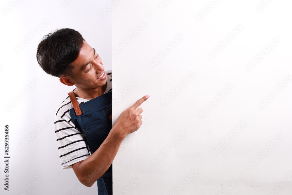 Happy Asian man in apron pointing something on white advertisement board on white background Happy Asian man in apron pointing something on white advertisement board on white background