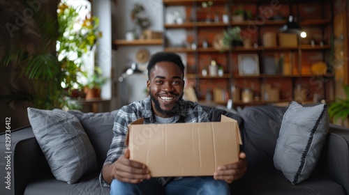 A cheerful man displays a cardboard box at home, signifying delivery and satisfaction © AS Photo Family