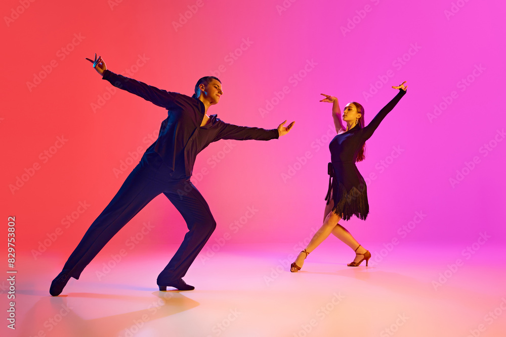 Pair of dancers in elegant poses in neon lighting against gradient background. Couple perform passionate Latin dance.Concept of dance and music, professional sport, action, competition, classical. Ad