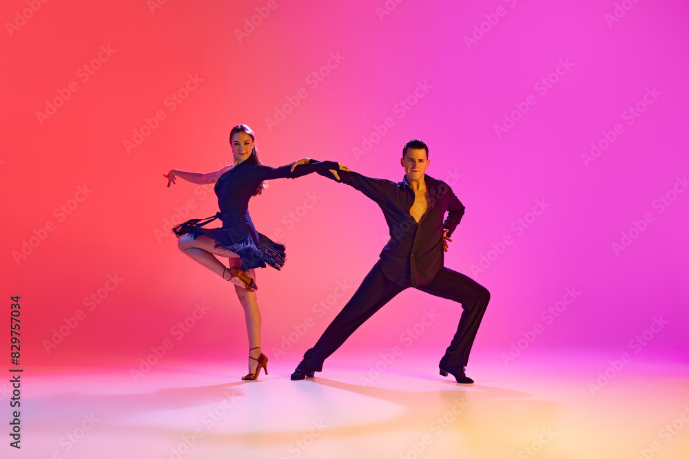 Young man and woman, ballroom dancers dancing expressively energetic Zumba in neon lighting against vibrant gradient background. Concept of dance and music, sport, action, competition, classical