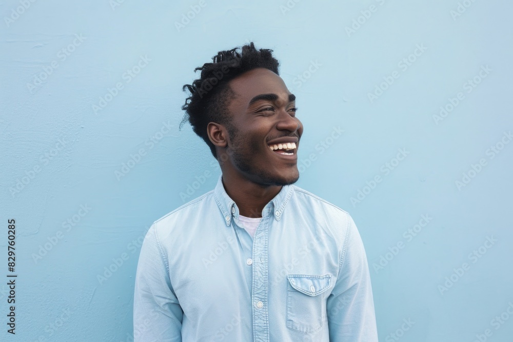 A man with a shaved head and a smile on his face is wearing a blue shirt. He is standing in front of a blue wall A man with a shaved head and a smile on his face is wearing a blue shirt. He is standing in front of a blue wall