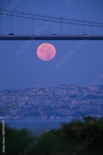 Full moon over Bosphorus bridge at night in Istanbul. The bright and full moon dominates the sky. Perfect for themes related to astronomy, lunar phases, and celestial events.