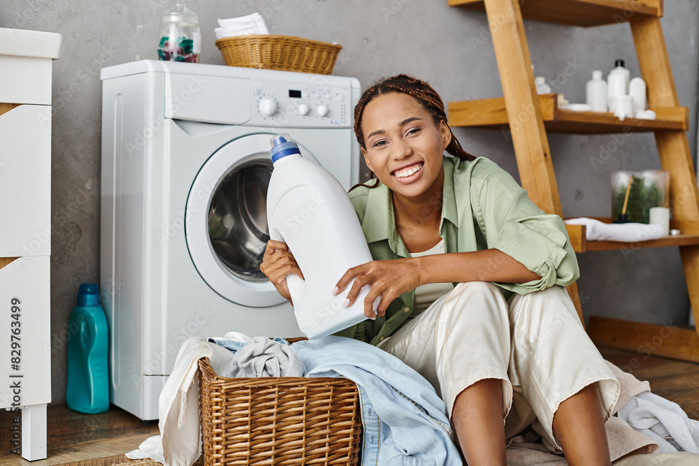 An African American woman with afro braids sits next to a washing machine, doing laundry in a bathroom setting. An African American woman with afro braids sits next to a washing machine, doing laundry in a bathroom setting.