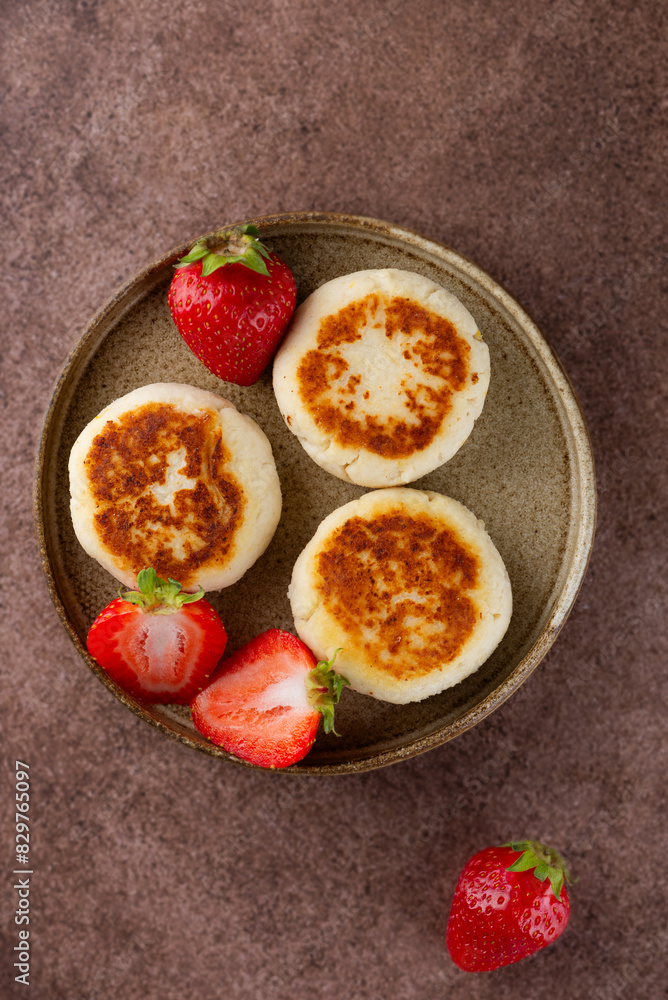 Cheesecakes, syrniki, cheese pancakes with strawberries, jam, cashew and tofu on a brown table. Sugar, lactose and gluten free. Vertical orientation, top view. Cheesecakes, syrniki, cheese pancakes with strawberries, jam, cashew and tofu on a brown table. Sugar, lactose and gluten free. Vertical orientation, top view.