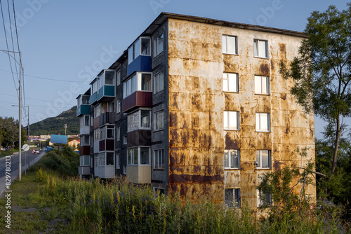 View of the old residential panel building. Rust on the metal wall of the house. Glazed balconies. Street of a provincial town in the Russian Far East. Real estate in the regions of Russia.