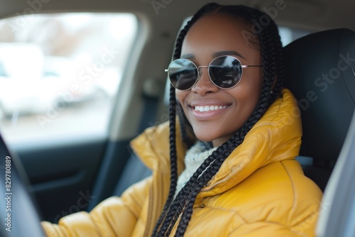 A woman with dreadlocks and sunglasses is smiling while driving a car. She is wearing a yellow jacket and she is enjoying her time in the car © vefimov