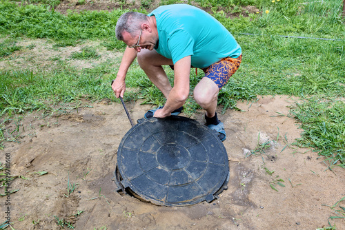 Man lifts manhole cover with crowbar to service drainage well.