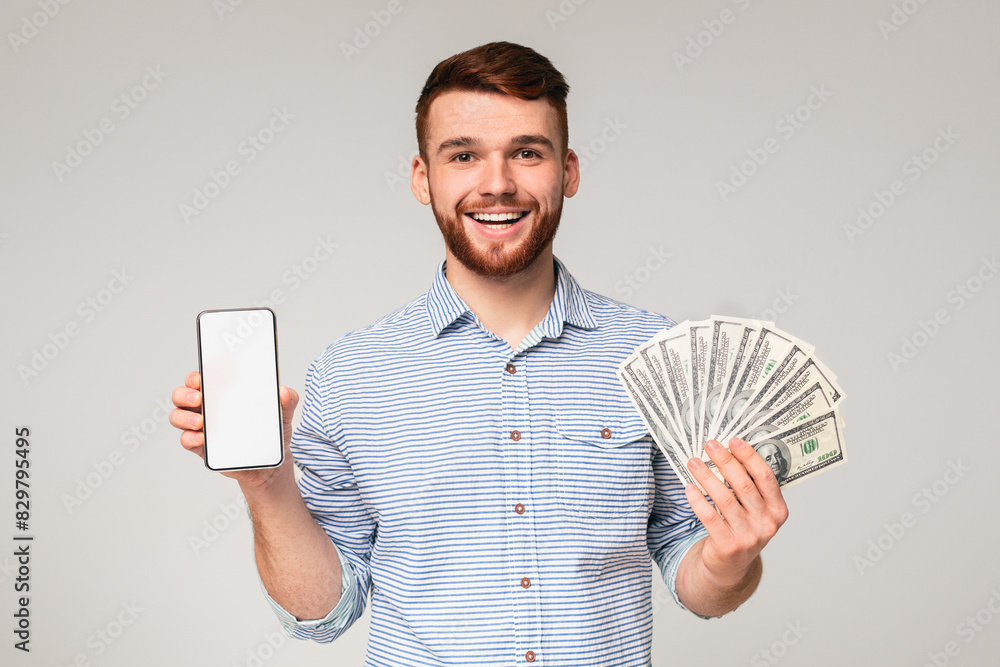 Freelance work. Handsome guy with cellphone with blank screen and fan of dollars on grey studio background, mockup