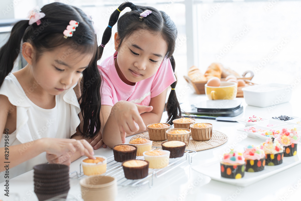Asian two children enjoy making cupcakes together at home kitchen. Little cute child girls pressing fresh baked cake texture, looking with smiling at homemade cupcake. Happy with holiday activities Asian two children enjoy making cupcakes together at home kitchen. Little cute child girls pressing fresh baked cake texture, looking with smiling at homemade cupcake. Happy with holiday activities