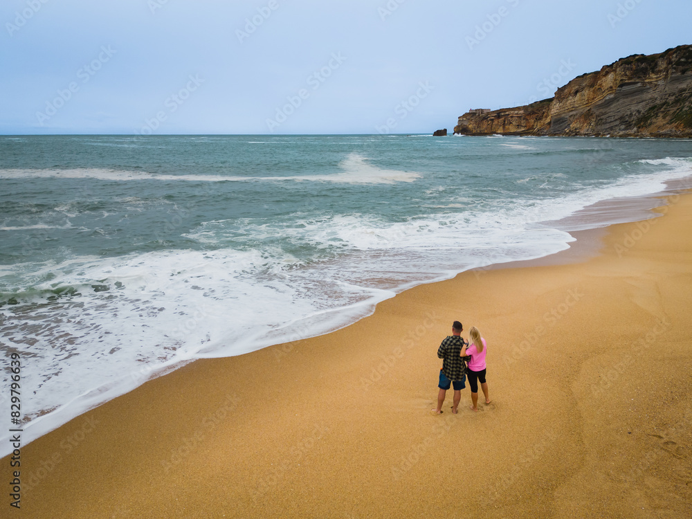 Romantic story. A young couple stands on the Nazare beach near the ocean, photo from a drone. Romantic story. A young couple stands on the Nazare beach near the ocean, photo from a drone.