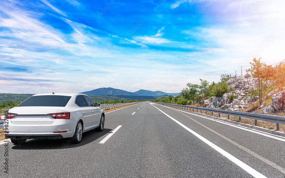 A white car drives along the highway against the backdrop of rocky mountains on a sunny day. A white car drives along the highway against the backdrop of rocky mountains on a sunny day.