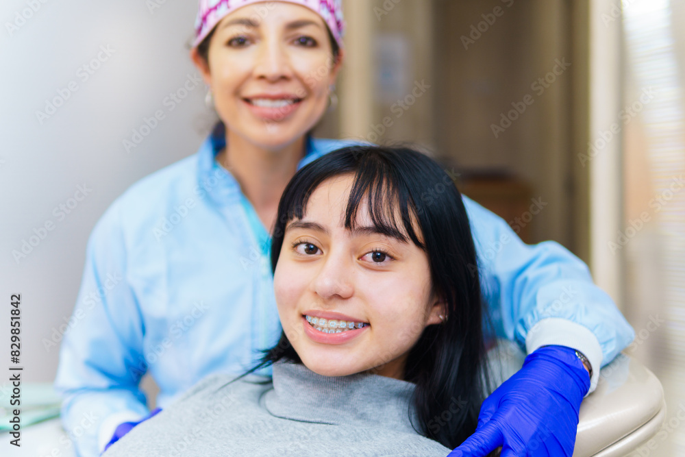 Close-up of a girl smiling and looking at the camera and in the background her orthodontist in a dental office Close-up of a girl smiling and looking at the camera and in the background her orthodontist in a dental office