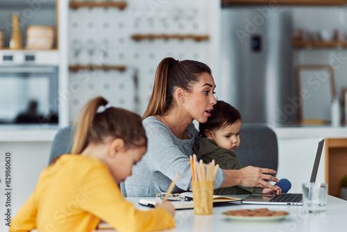 A hard-working mother having a video call on her laptop while working from home and looking after her kids
