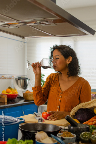 Young woman enjoys a glass of wine in the kitchen at home while cooking