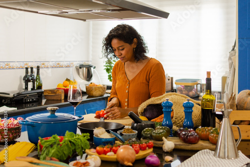 Young brunette woman cutting a fresh tomato on a cutting board in the kitchen at home