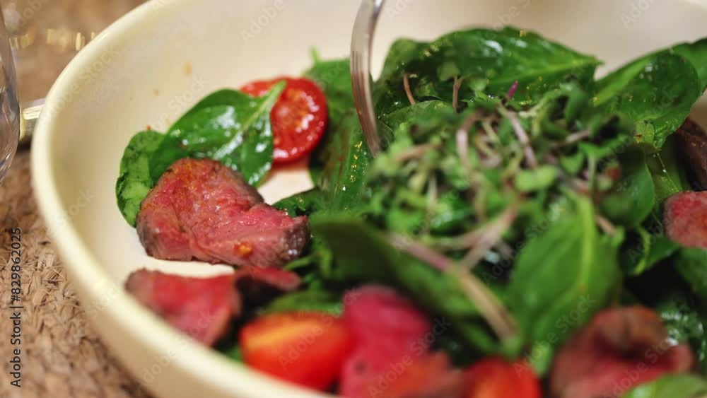 Anonymous restaurant customer checking ingredients of served warm salad in white ceramic bowl. Delicious starter consisting of roasted beef slices, halved cherry tomatoes and mix of micro green. Anonymous restaurant customer checking ingredients of served warm salad in white ceramic bowl. Delicious starter consisting of roasted beef slices, halved cherry tomatoes and mix of micro green.