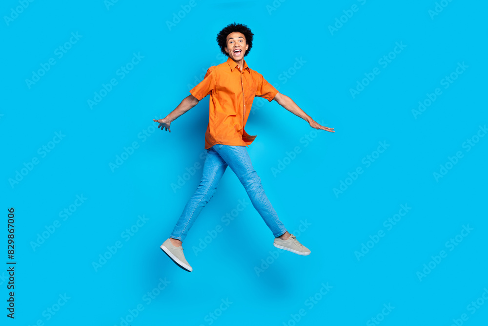 Full length photo of cheerful positive guy dressed orange shirt walking jumping high empty space isolated blue color background Full length photo of cheerful positive guy dressed orange shirt walking jumping high empty space isolated blue color background