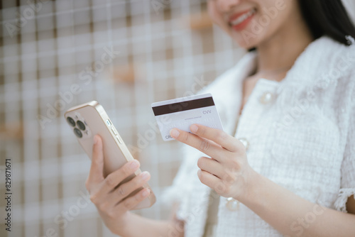 Attractive millennia Asian female holding her smartphone and credit card, using mobile banking app or online shopping app. photo