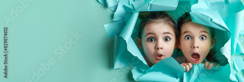 Happy multiethnic children looking at camera and amazed behind hole in solid paper background celebrating International Children's Day