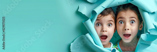 Happy multiethnic children looking at camera and amazed behind hole in solid paper background celebrating International Children's Day