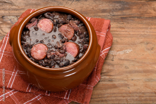 FEIJOADA IN A BROWN BOWL ON A WOODEN BASE.