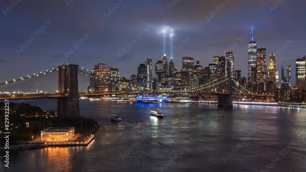 Ethereal twin beams of the September 11th Tribute in Light illuminating passing clouds in Lower Manhattan. Night view of Brooklyn Bridge, East River and financial district skyscrapers. New York City Ethereal twin beams of the September 11th Tribute in Light illuminating passing clouds in Lower Manhattan. Night view of Brooklyn Bridge, East River and financial district skyscrapers. New York City