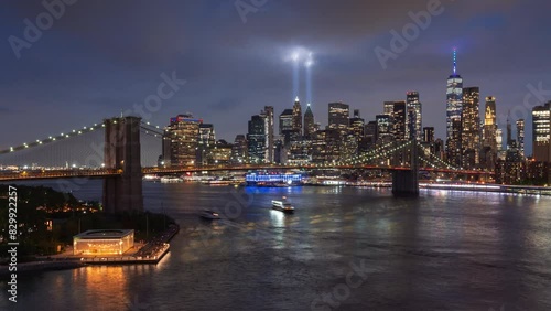 Ethereal twin beams of the September 11th Tribute in Light illuminating passing clouds in Lower Manhattan. Night view of Brooklyn Bridge, East River and financial district skyscrapers. New York City